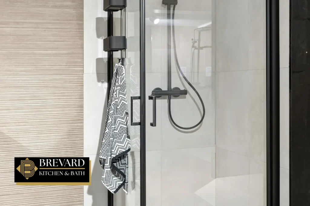 Curbless shower with a black handheld shower head and glass panel